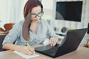 Young clever woman writing notes at laptop