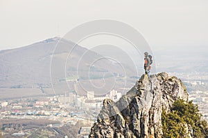 A young climber looking out of the top of a steep cliff against the background of caucasian city and mountains