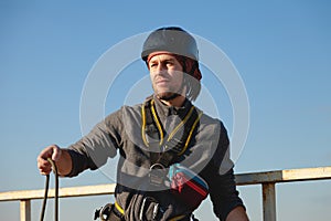 A young climber unwinds a safety rope on the roof of a building. Sunny weather, handsome man squinting