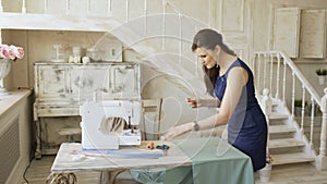 Young clothing designer and seamstress woman sew with thread and needle near sewing machine