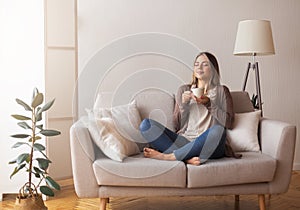 Young coffee lover sniffing hot drink at cozy home interior photo