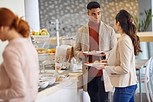 Young colleagues talking while picking a food at company canteen. People, job, company, business concept