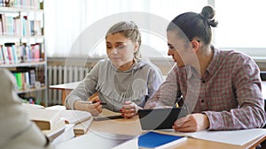 Young college students working together using tablet and discussng project preparing for exams while sitting at table at