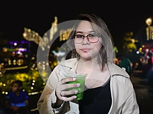 Young Colombian Hispanic girl in a fair of lights drinking a green juice