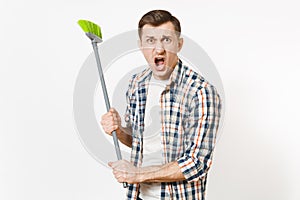 Young combative angry housekeeper man in checkered shirt holding and sweeping with green broom isolated on white