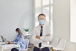 Young company worker wearing face mask standing in his workplace looking at camera