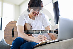 Young composer man composing song with guitar and laptop at home. Selective focus of musician's hand