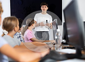 Young computer science teacher standing near an interactive whiteboard tells new material to teenage students in school