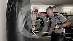 Young concentrated african male boxer hitting punching bag in boxing club