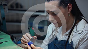 Young concentrated female jeweller working with equipment in workshop indoors. Portrait of Caucasian woman with tool