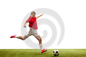 Young concentrated girl, football player in motion, playing on green grass, ready to hit ball isolated on white