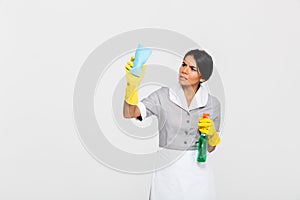 Young concentrated maid in uniform cleaning window with rag