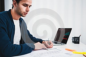 Young concentrated male architect working on new building blueprint plan using modern laptop with digital trend and graph in offic