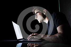Young concentrated man using laptop computer at home indoors at night looking at laptop white screen