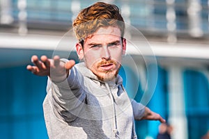 Young concentrated red-haired man practicing exercise with a sweatshirt during the day and earrings on his ears, close-up portrait