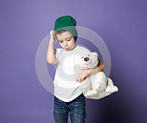 Young concerned kid boy child in green hat holding his polar bear toy. International day of polar bear concept