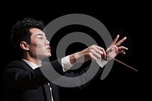 Young conductor with baton raised, black background