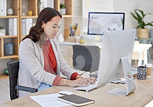 Young confident asian business woman sitting alone in an office and browsing the internet on a computer. Ambitious
