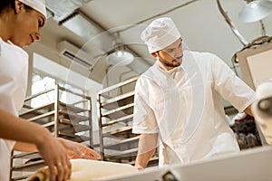 young confident bakers working with industrial dough roller