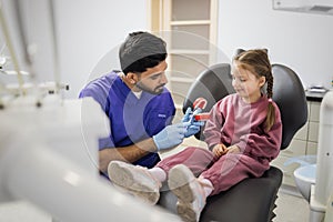 Young confident bearded pediatric dentist showing to little preschool girl how to brush teeth