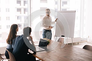 Young confident businessman presenting new project to partners on whiteboard