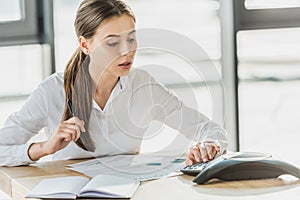 young confident businesswoman with paperwork using conference phone