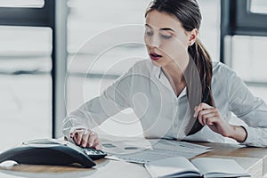 young confident businesswoman with paperwork using conference phone