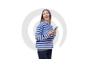 young confident european brunette woman dressed in striped blue clothes holding a smartphone in her hand