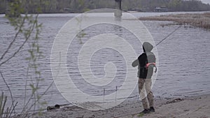 Young confident fisherman in khaki pants in the early morning spinning fishing in river near the city. Fishing rod and a