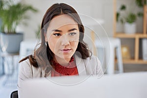 Young confident focused asian business woman sitting alone in an office and browsing the internet on a computer