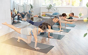 Young confident girl with group of active multinational people doing stretching exercises during yoga class