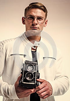 young confident guy in white urban clothes making photo with retro camera, fashion photographer