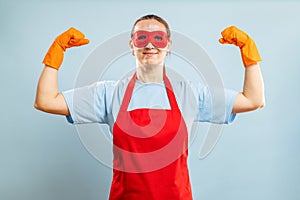 Young confident housewife in cleaning superhero costume on blue background