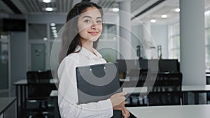 Young confident Indian businesswoman model posing indoors smiling female manager office worker trainee stands holding