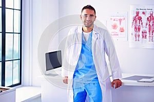 Young and confident male doctor portrait standing in medical office.