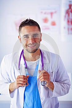 Young and confident male doctor portrait standing in medical office.