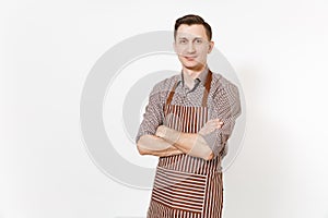 Young confident man chef or waiter holding hands crossed in striped brown apron, shirt isolated on white background