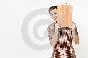 Young confident man chef or waiter in striped brown apron, shirt holding wooden cutting board, knife isolated on white