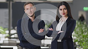 Young confident man and woman business partners smiling confidently to camera, posing with crossed arms at modern office