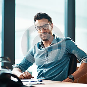 Young, confident and professional business man wearing glasses, sitting at his desk and working in a modern office