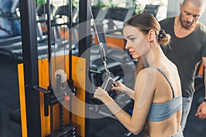 Young, confident, slim, caucasian woman with blond hair in a bun, wearing a grey gym set, doing cable tricep extensions