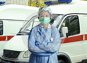 Young confident and successful Asian Korean medicine doctor woman in hospital scrubs and mask posing outdoors with ER ambulance