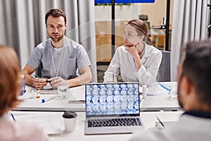 Young confident surgeon looking at one of colleagues during medical concilium