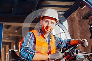 Young confident warehouse worker posing in a forklift truck