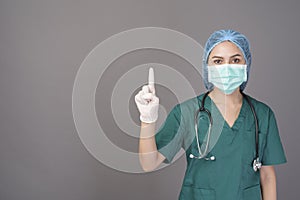 Young confident woman doctor in green scrubs is wearing surgical mask over grey background studio