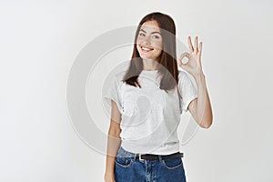 Young confident woman standing on white background and showing okay sign, confirm and approve something, praise good