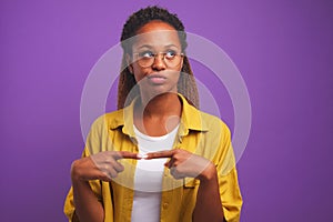 Young confused African American woman in round glasses with smirk looks up