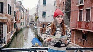 A young confused woman standing above the water channel and looking at the map - Venice, Italy