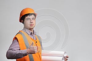 Young construction worker in hard hat showing thumbs up class sign on grey studio background