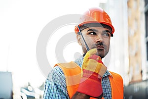 Young construction worker in uniform using walkie talkie on site